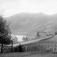 07.10.1909. Parti fra Bredebygden. Bebyggelse, vei, gjerder, mann ved port, åsside med bebyggelse og skog, elv.
