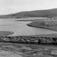 Oversiktsbilde over Klokkerklemets gård med bygninger, og vannet i forgrunnen. Avzze, Kautokeino, Finnmark, 1953.
