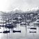 Bilde fra Lofoten. Bebyggelse på nes, båter på havnen og fjell med snø i bakgrunnen.